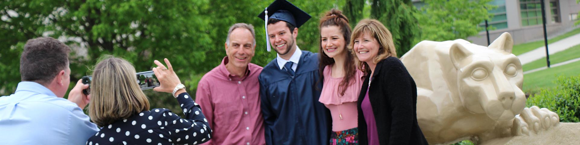 Student with family by the Nittany Lion Shrine getting picture taken during graduation